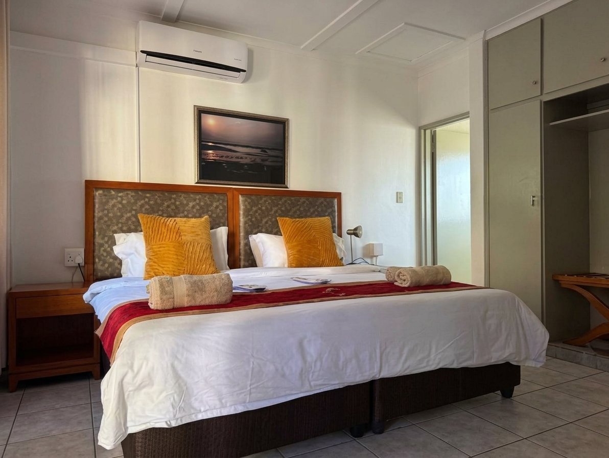 Modern bedroom with wooden headboard bed, white bedding, gold decorative pillows, and air conditioning unit on the wall