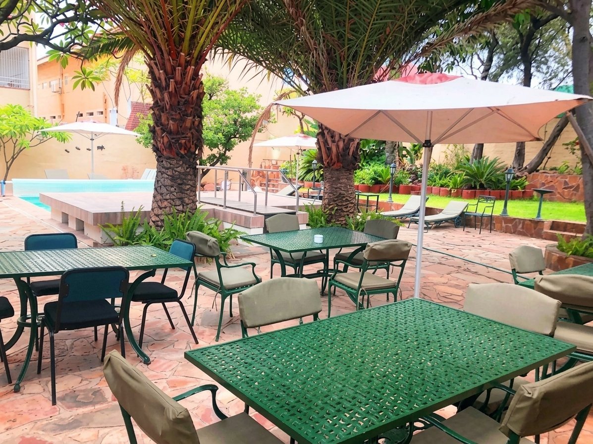 Outdoor patio area with green dining tables, lounge chairs, umbrellas, palm trees, and a swimming pool visible in background