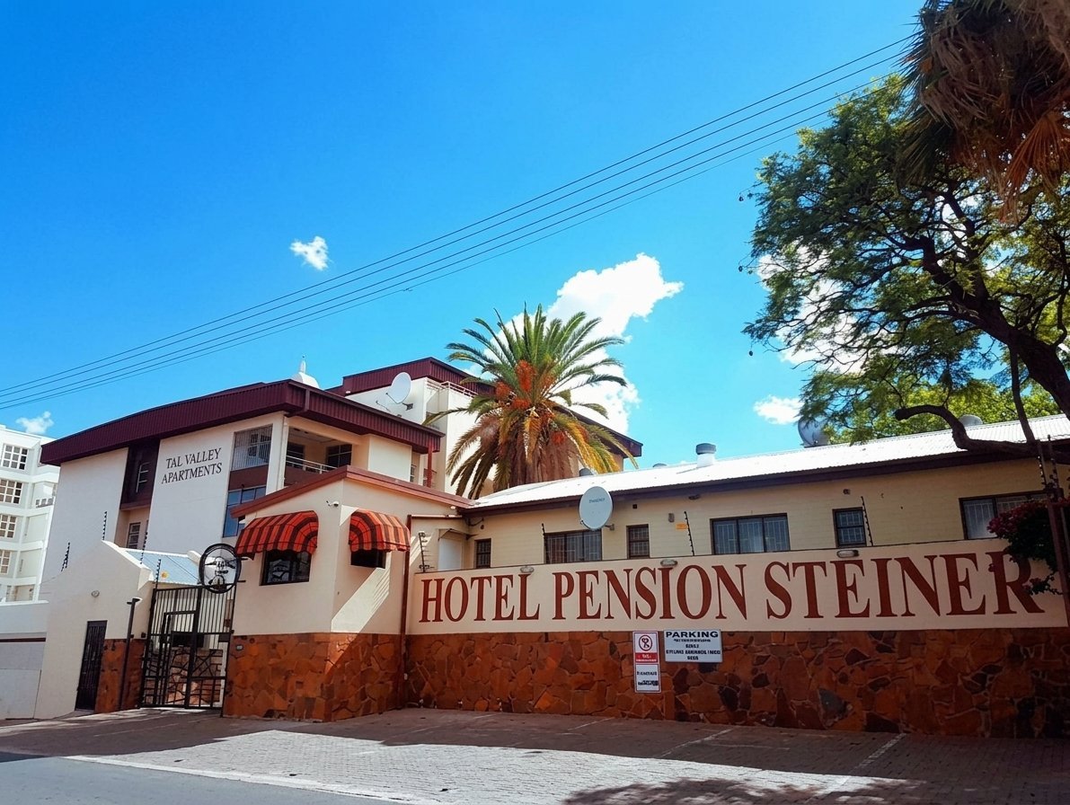 Hotel Pension Steiner exterior with palm tree, cream and burgundy facade, clear blue sky and green trees